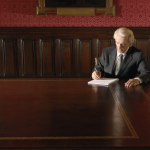 Man writing at large wooden desk.