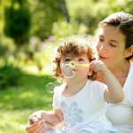 Child and woman blowing bubbles in park.