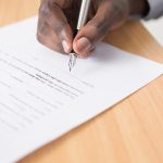 Hand signing a document with a pen.