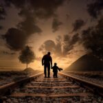 Silhouetted figures walking on railroad at sunset.