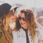 Two women laughing outdoors, wearing sunglasses.