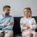 Man and woman sitting, arms crossed, serious.