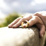 Hand wearing a gold ring on railing.