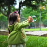 Child playing with bubbles in the park.
