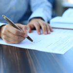 Person signing document with pen on table.