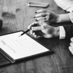 Hands reviewing a contract on table.