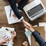 Handshake over business documents and laptop.