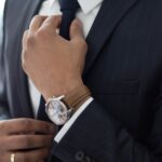 Man adjusting tie, wearing a wristwatch.