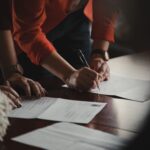 People signing documents on a wooden table.